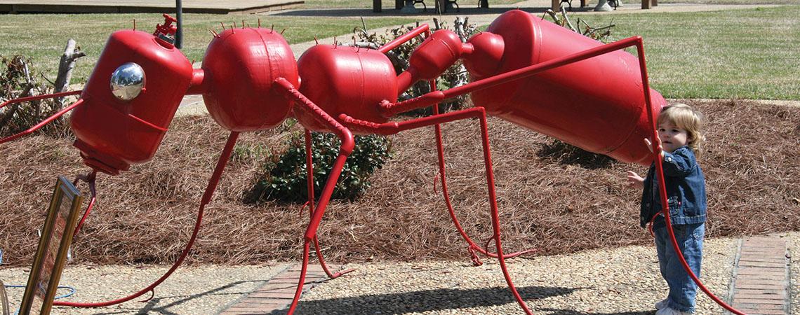 large, red ant sculpture with toddler for reference